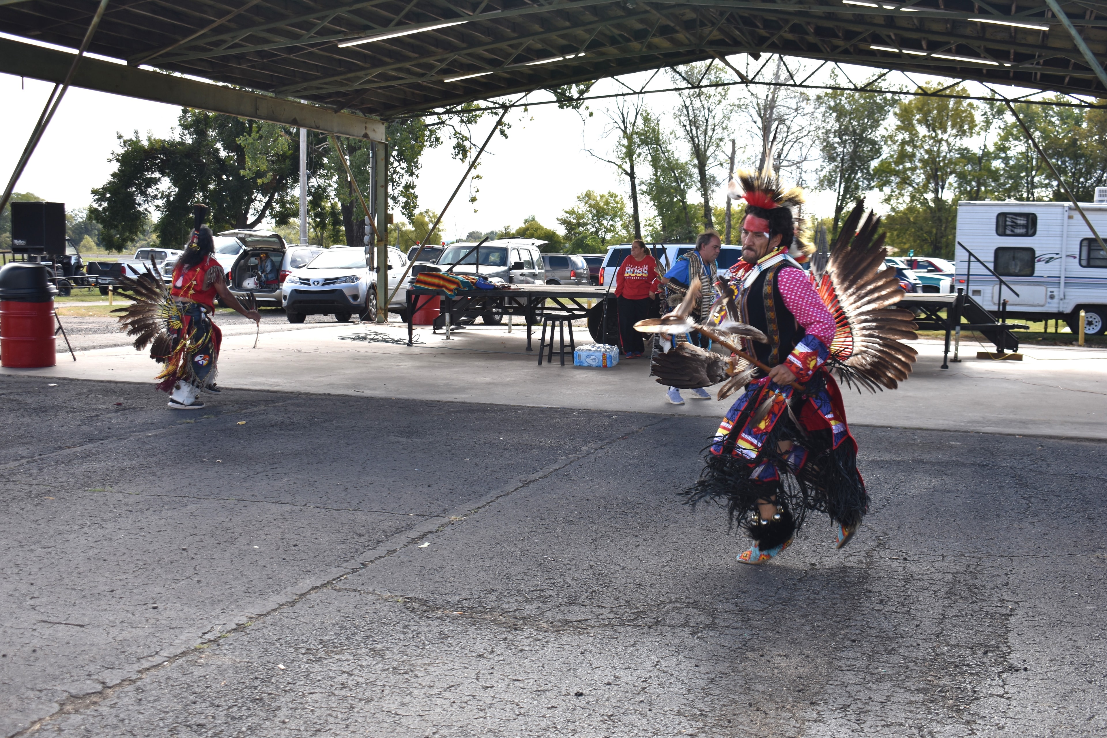Two Cherokee dancers in traditional regalia performing under a pavilion