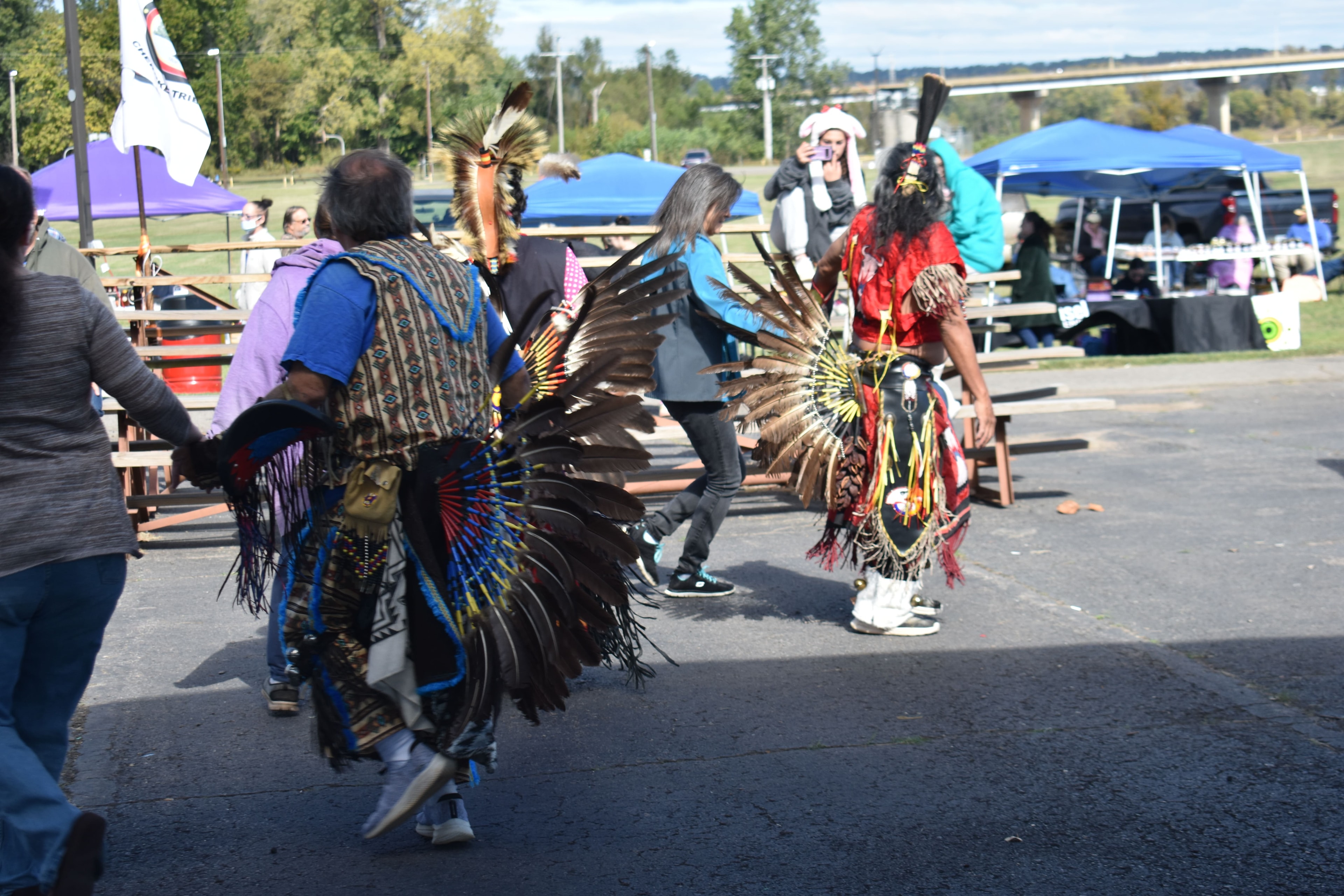 Cherokee dancers in traditional regalia with the tribal flag visible in the background
