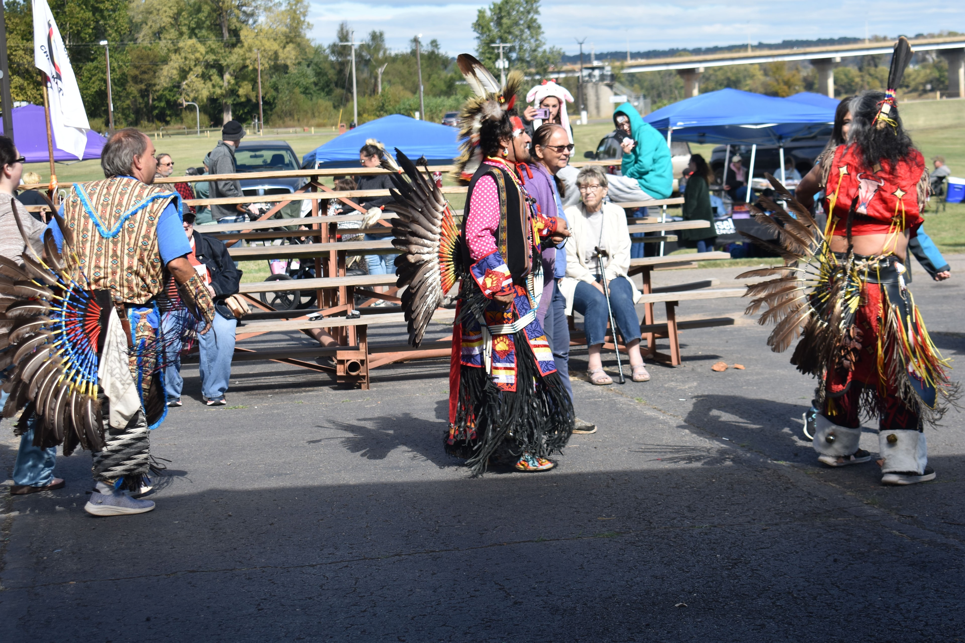 Three Cherokee dancers in traditional regalia performing for the crowd