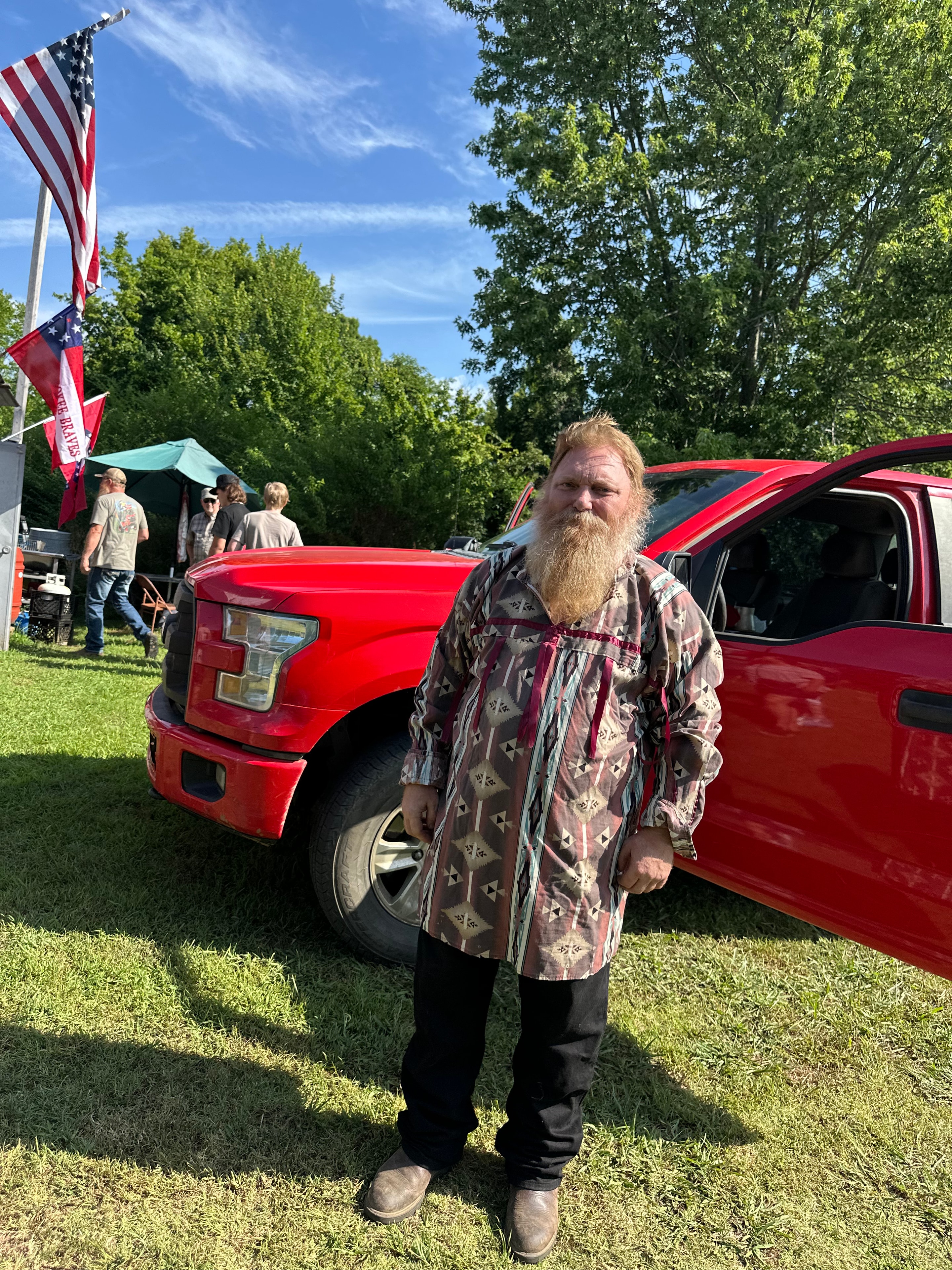 Tribal member in ribbon shirt standing by red truck at Green Tree Ceremony July 11, 2026